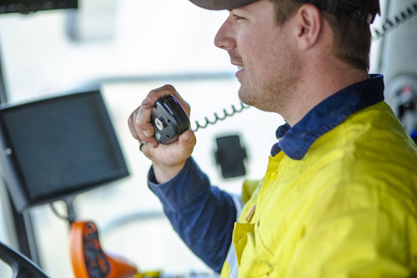 A man in a hi vis shirt speaks into a two radio in the cab of a harvester