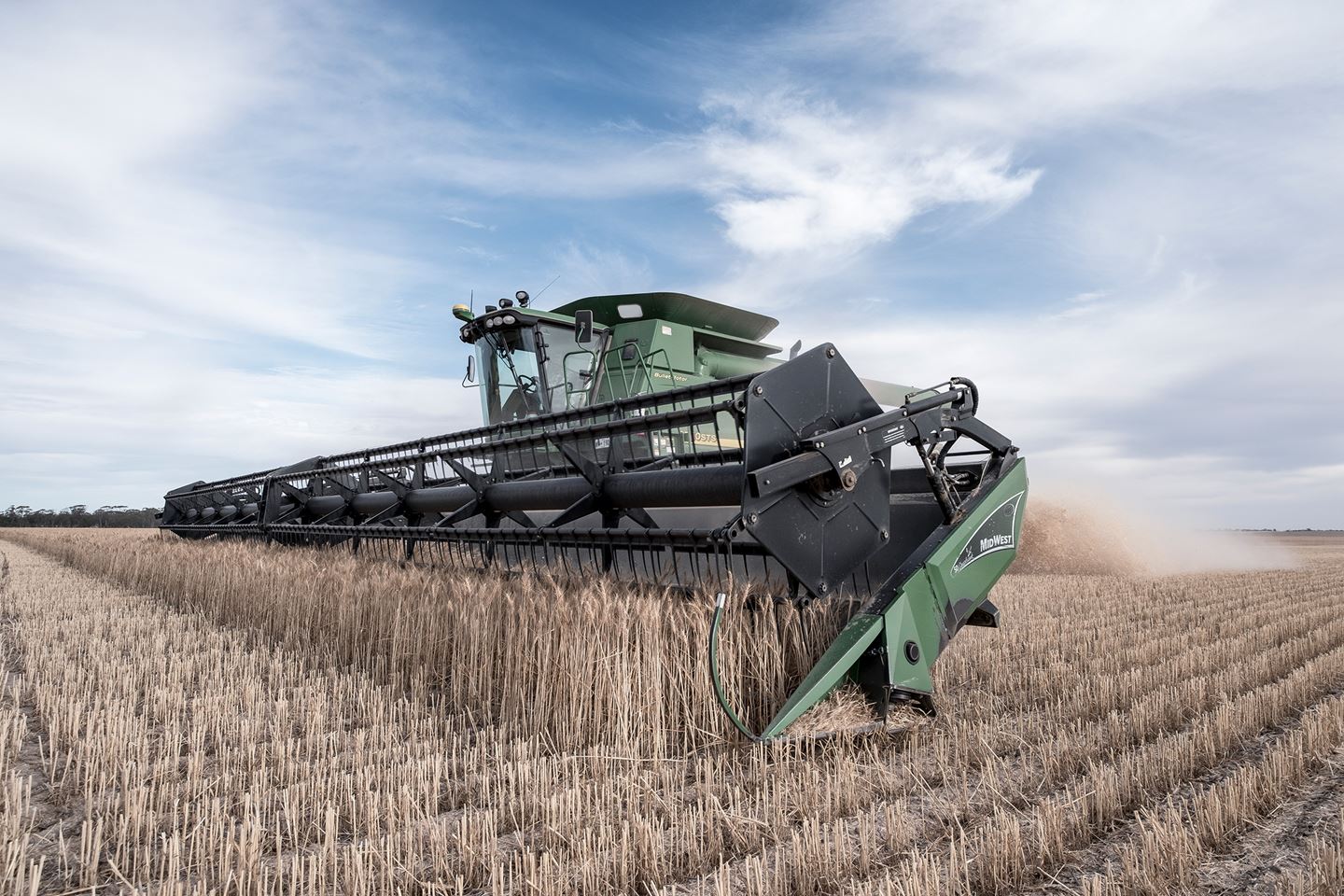 A close up of a green harvester in a paddock full of golden wheat