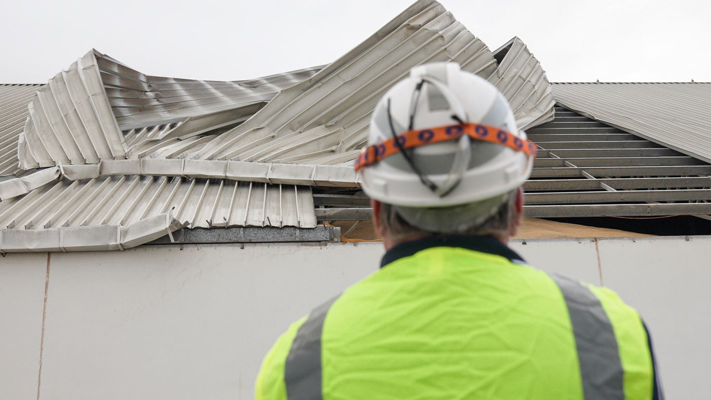 CBH employee in a hard hat look at a damaged tin roof on site