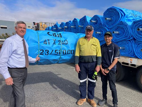 Three men stand in front of a truck loaded with tarps
