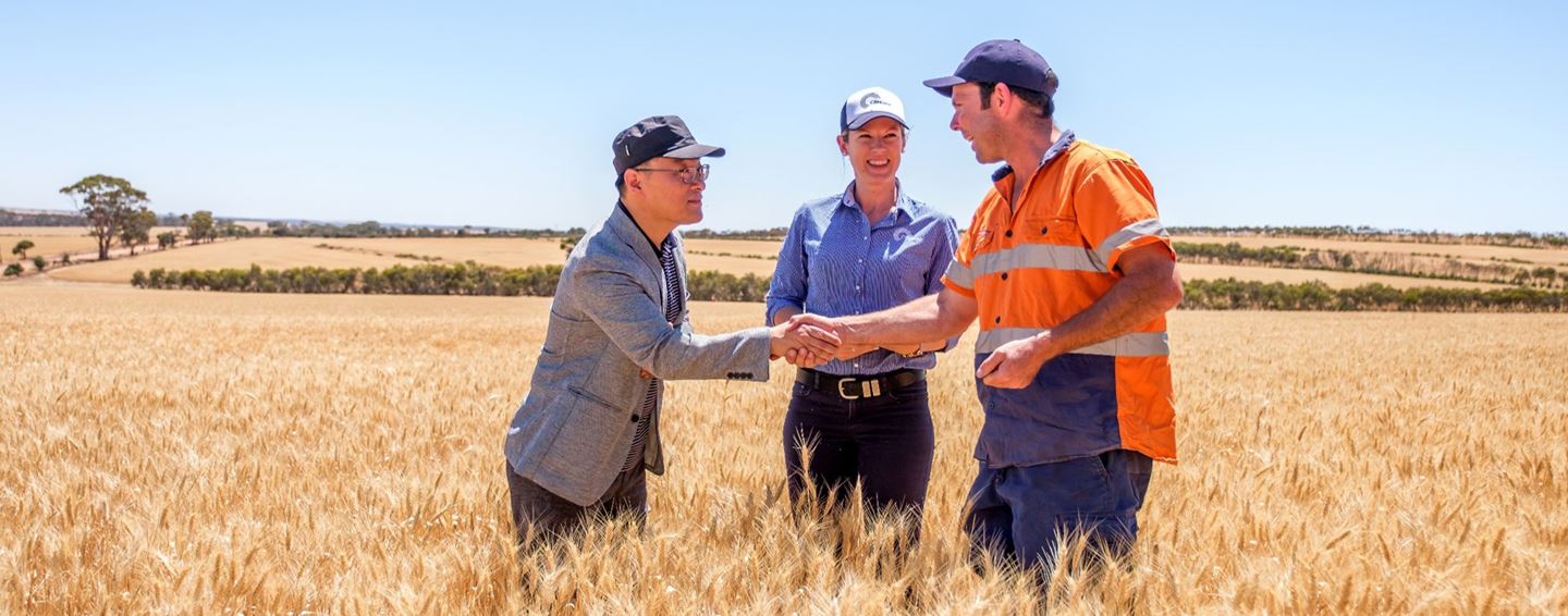 Two men shaking hands in a paddock while a woman looks on smiling