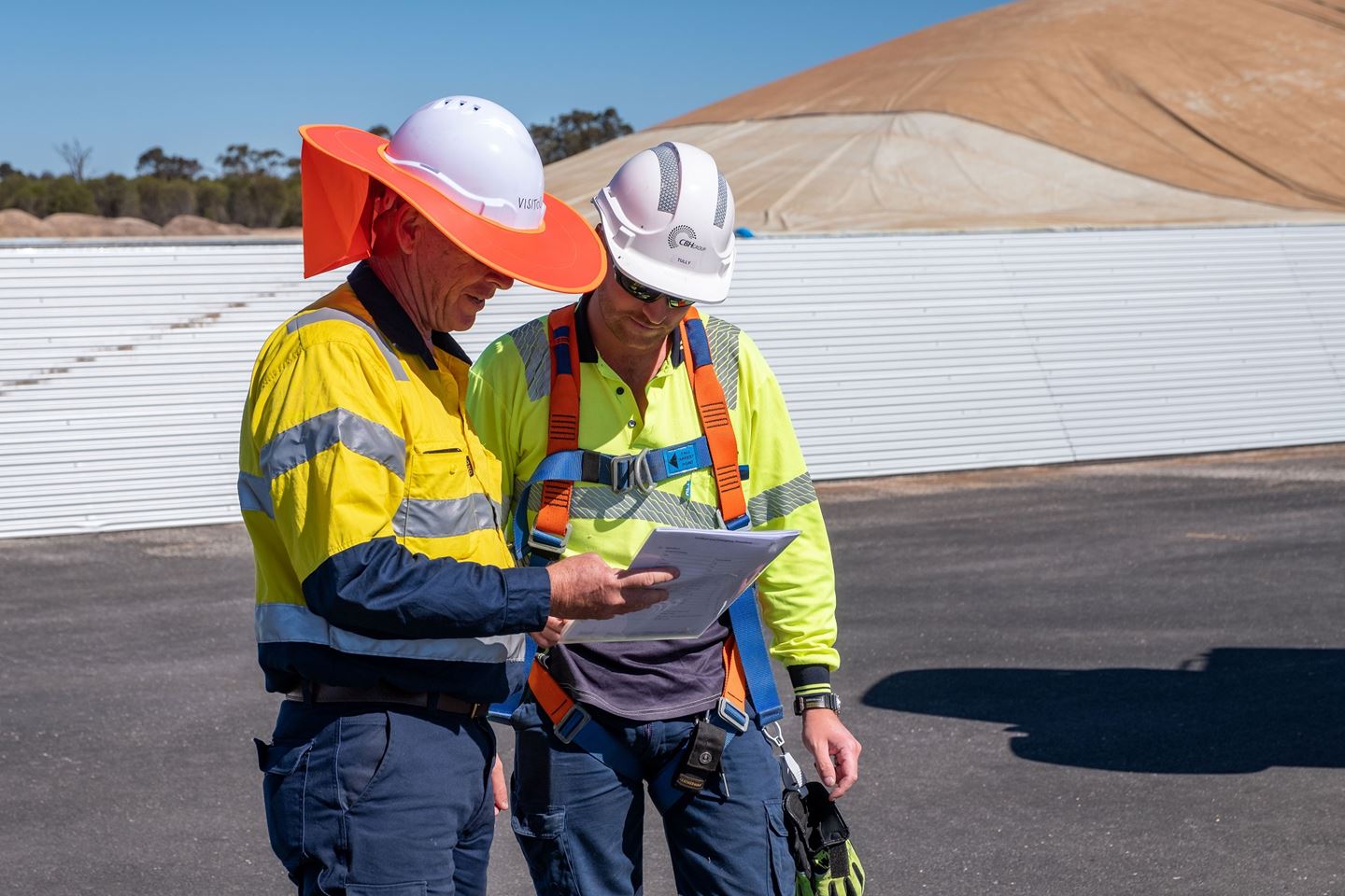 Two people wearing hard hats reading a clipboard