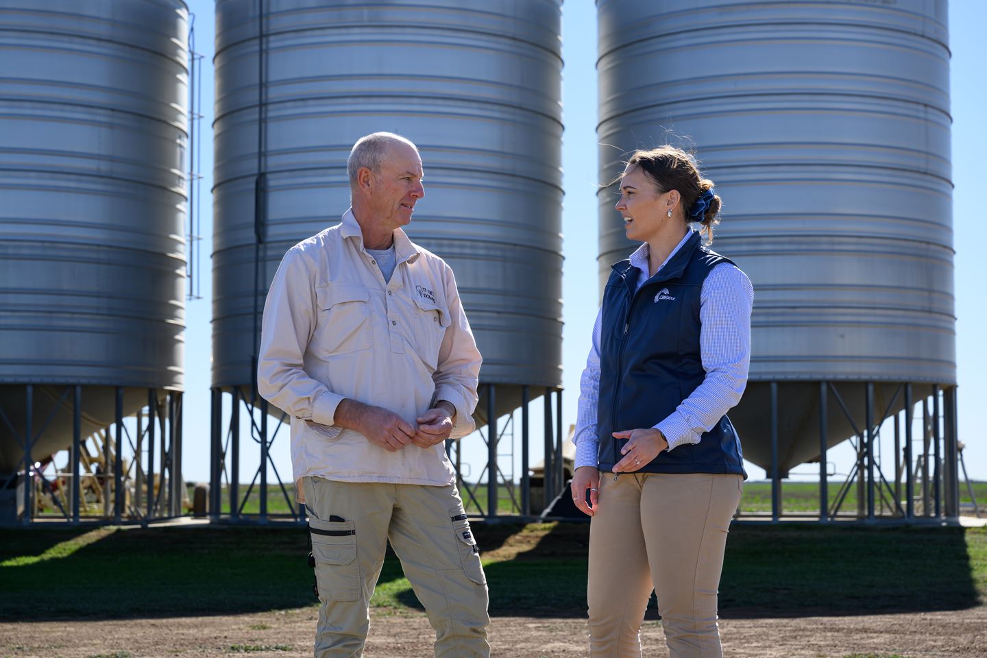 Two men in blue shirts standing in paddock inspecting crop